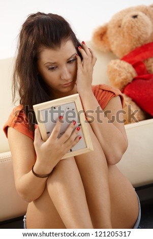Heart-broken young girl looking at ex-boyfriends photo crying.