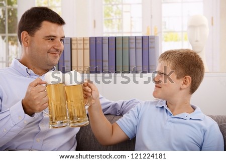 Father and son drinking beer, clinking with glasses, smiling.