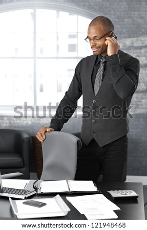 Businessman on mobile telephone call, standing at office desk, concentrating.