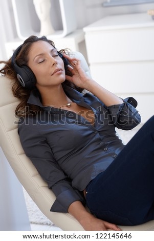 Pretty young woman sitting relaxed in chair, listening to music through headphones eyes closed.