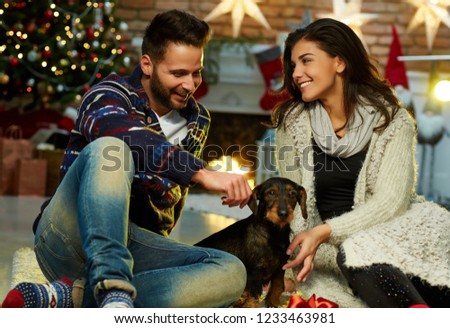 Christmas couple at home in Winter. Happy young couple sitting on floor at home with dog in Christmas time. Christmas tree and fireplace in background.