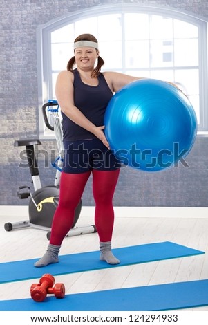 Happy fat woman exercising with fit ball at the gym, smiling.