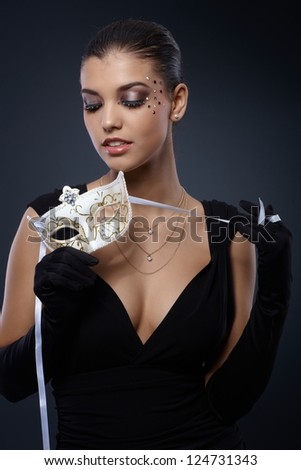 Beauty in smart black dress with carnival mask and party makeup.