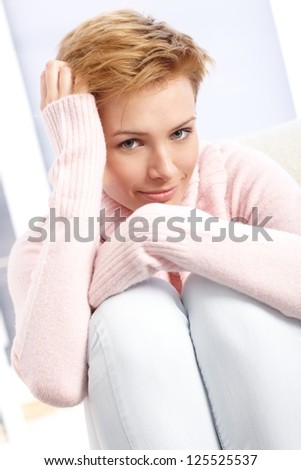 Smiling attractive woman hugging knees, hand in hair.