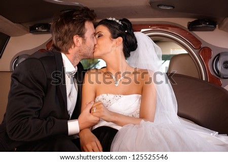 Bride and groom kissing in limousine on wedding-day.