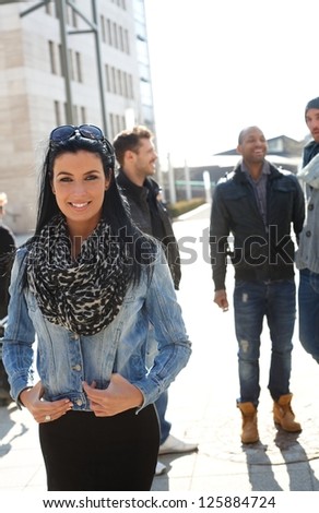 Attractive woman standing in springtime sunshine outside of building, group of guys in the background.