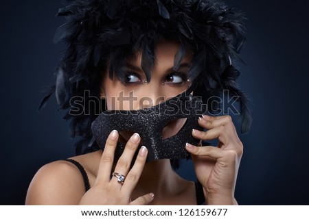 Girl hiding in glittering black carnival mask and feather boa, looking away.