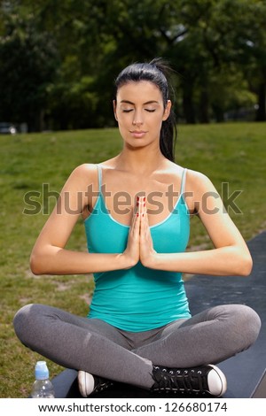 Pretty young woman practicing yoga in park, eyes closed, prayer position.