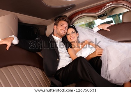 Beautiful young couple smiling happily on wedding-day, sitting in limousine.