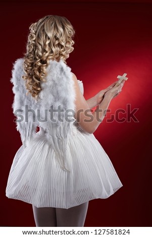 Back view of blonde woman dressed like an angel holding crucifix.