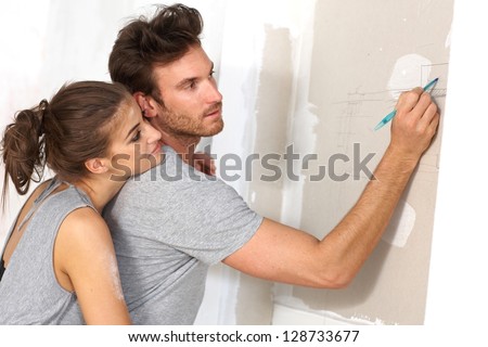 Young couple planning new home, drawing floor plan on wall, hugging.