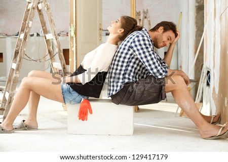 Exhausted couple sitting in house under construction back to back.