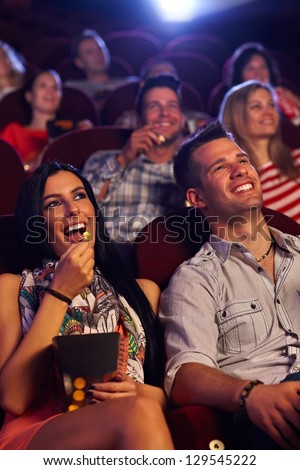 Young Couple Sitting In Cinema, Watching Movie, Eating Popcorn, Smiling.