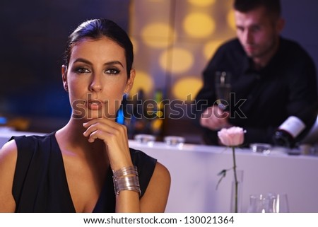 Evening portrait of elegant young woman in restaurant. Man at background.