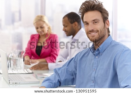 Portrait of handsome young businessman sitting at a meeting, smiling confident.