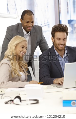 Happy young businesspeople working together in bright office, using laptop computer, smiling.