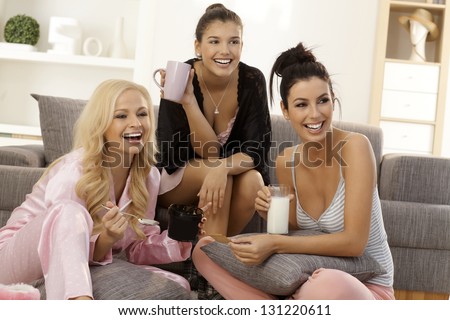 Girls together at home, watching tv in pyjamas, smiling happy.