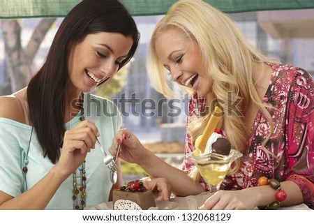 Pretty female friends sharing a chocolate cake at outdoor cafe, smiling happy.