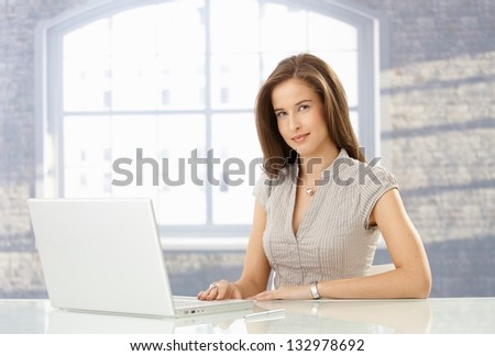 Attractive woman sitting at table with laptop computer, looking at camera.