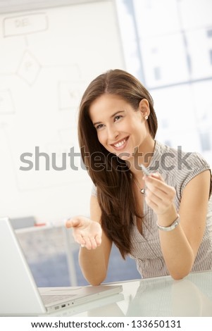 Laughing businesswoman sitting at meeting table with laptop computer, gesturing.