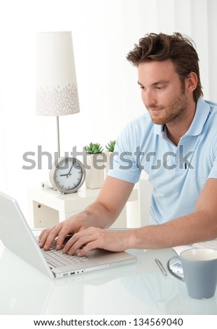 Handsome man typing on laptop computer keyboard, looking at screen, smiling.