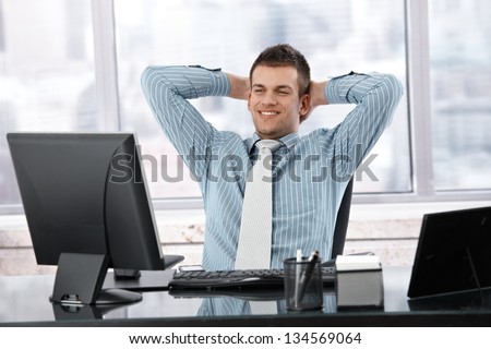 Satisfied businessman sitting at desk in bright office, looking at screen.