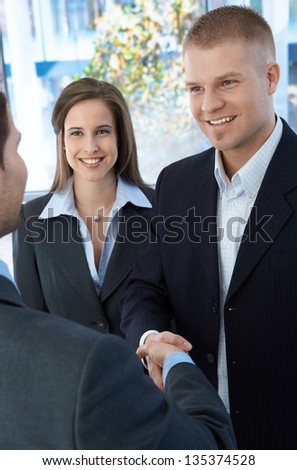 Business colleagues introducing with handshake, standing in office, smiling.