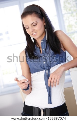 Young female using mobile phone at home, smiling.