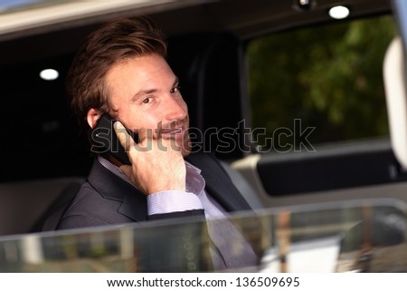 Handsome young businessman on phone call, sitting in elegant car.