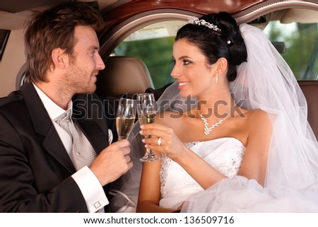 Bride and groom sitting in limousine, clinking glasses on wedding-day.