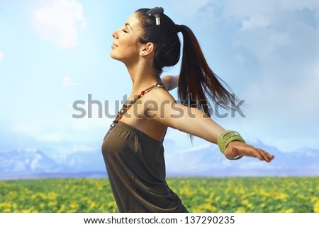 Attractive young woman enjoying summer sun and wind on the meadow. Side view, pretending to fly.