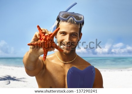 Happy young scuba diver holding sea star, smiling, looking at camera.
