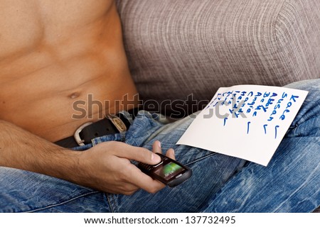 Portrait of semi-nude athletic male body, using mobile phone and piece of paper with list of female names.