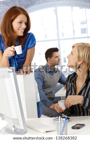Coffee break in office, businesswomen chatting, holding coffee cup, smiling.