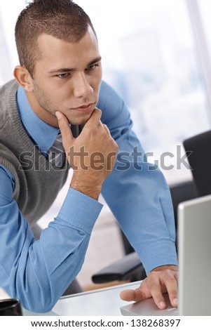 Businessman thinking, leaning in looking at computer work, serious and determined.