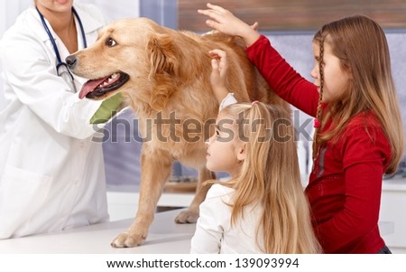 Little sisters and dog at veterinary surgeon, vet examining dog.