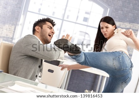 Young couple fighting, woman kicking man. Relationship crisis. Stress at workplace.
