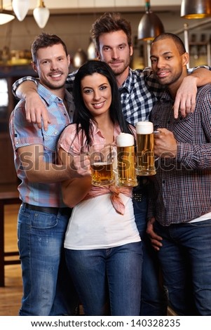 Group of happy young friends drinking beer at pub, smiling, clinking glasses