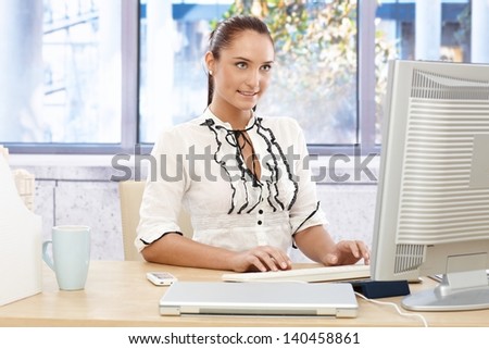 Happy businesswoman busy working on desktop computer, looking at monitor, typing.