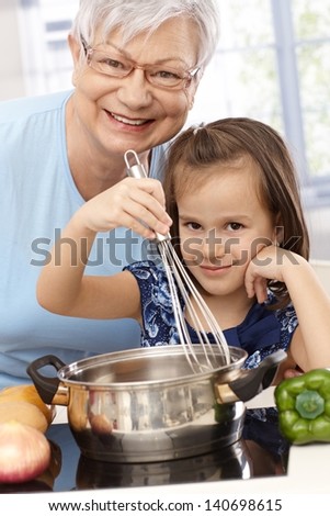 Grandmother and little granddaughter cooking at home, smiling.