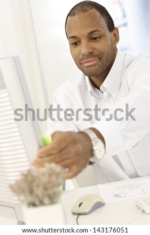 Portrait of young Afro-american businessman sitting at desk, working with computer in office.