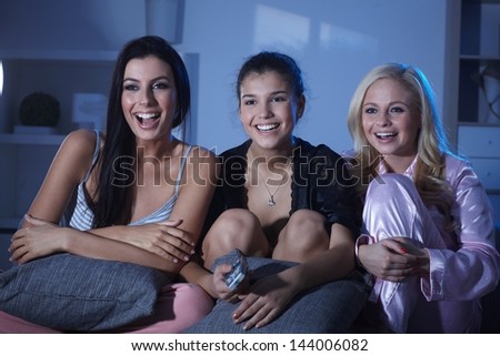 Happy roommates watching tv at home at night, wearing pyjamas, smiling happy.