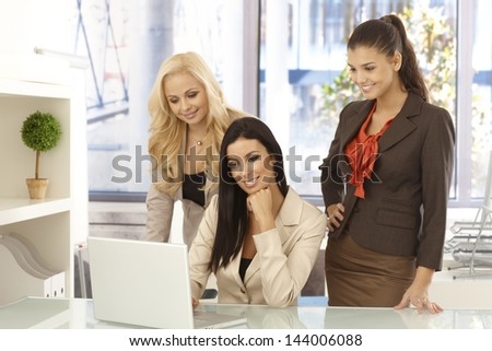 Happy businesswomen working together on computer at desk, smiling.
