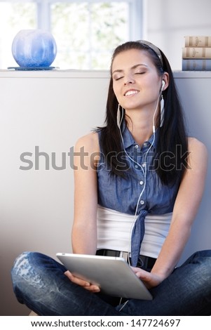 Pretty girl enjoying music through headset and tablet, eyes closed smiling.
