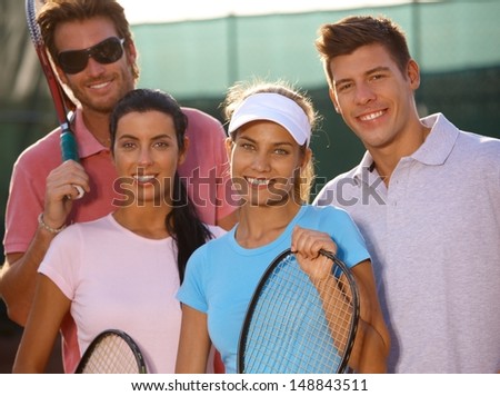 Portrait of smiling young tennis team on tennis court.