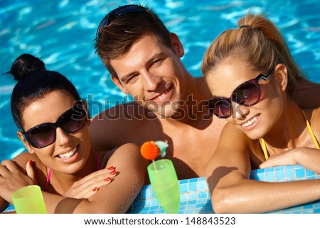 Attractive young people smiling in swimming pool, drinking cocktail.