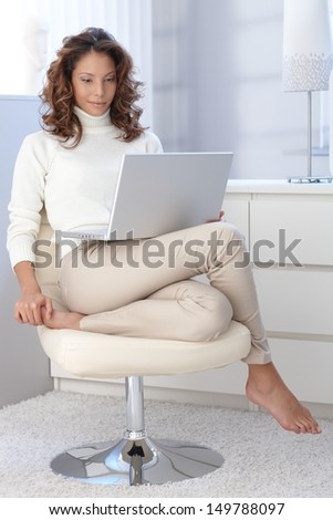 Pretty woman using laptop computer, sitting in modern chair at home.