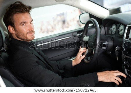 Handsome young man sitting in luxury car, looking at camera.