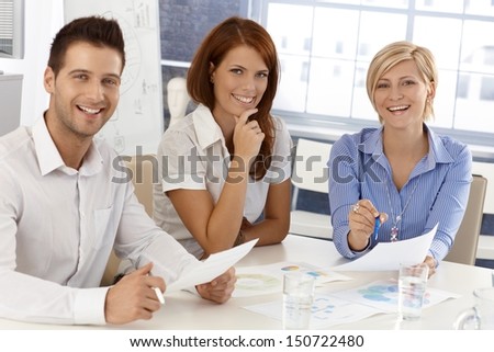 Happy businessteam at meeting, working with documents, laughing, looking at camera.