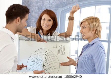 Happy businessteam discussing diagram on whiteboard in meeting room, smiling.